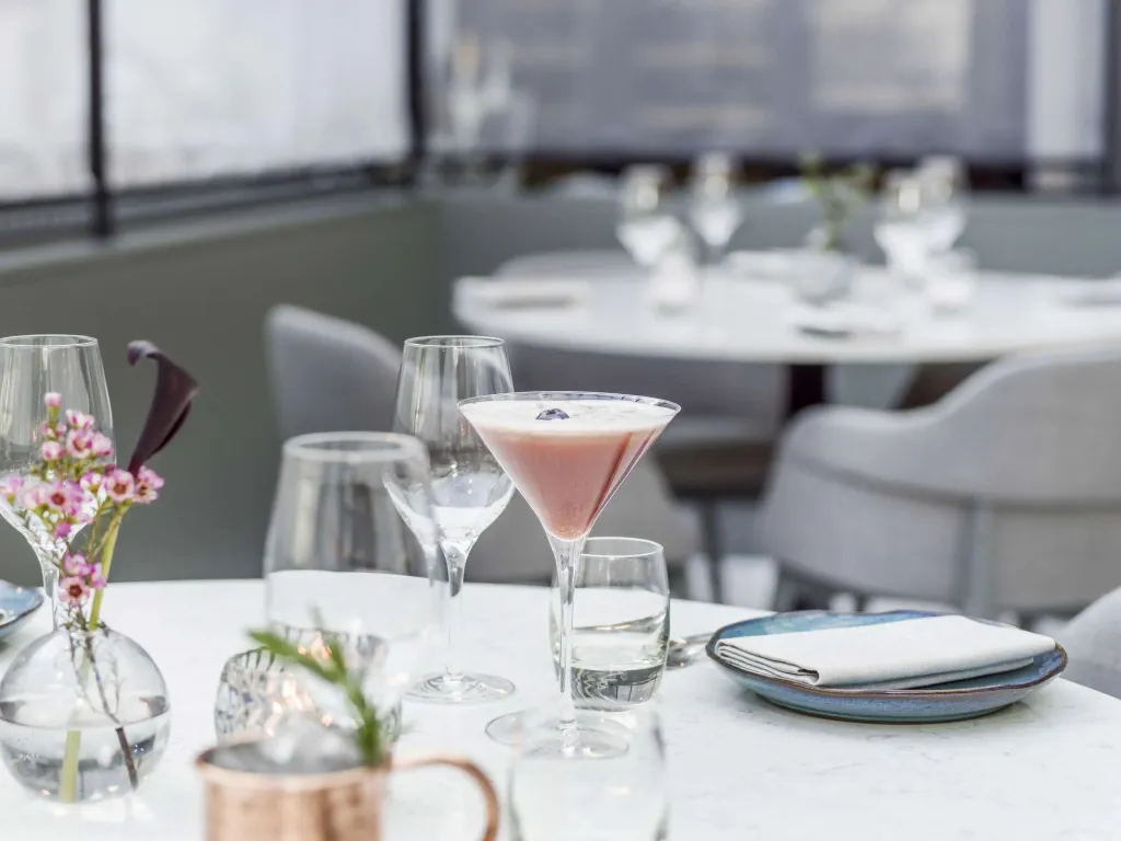 Une table dressée avec des verres et une boisson colorée dans un espace lumineux.