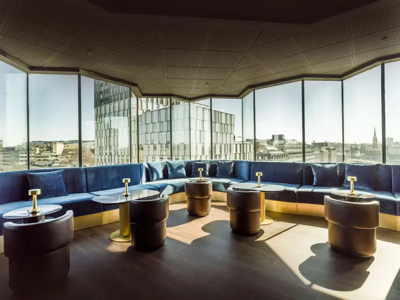 Un espace de détente intérieur avec des banquettes bleues et des tables basses rondes offre une vue sur la ville.