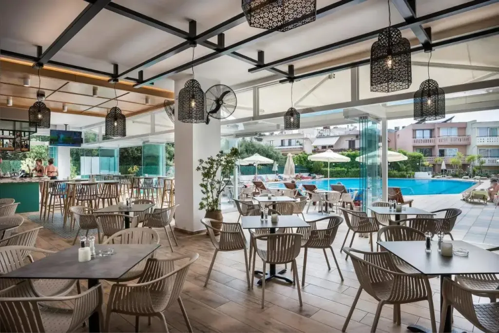 Une salle lumineuse avec un bar et des tables de repas donnant sur une piscine.