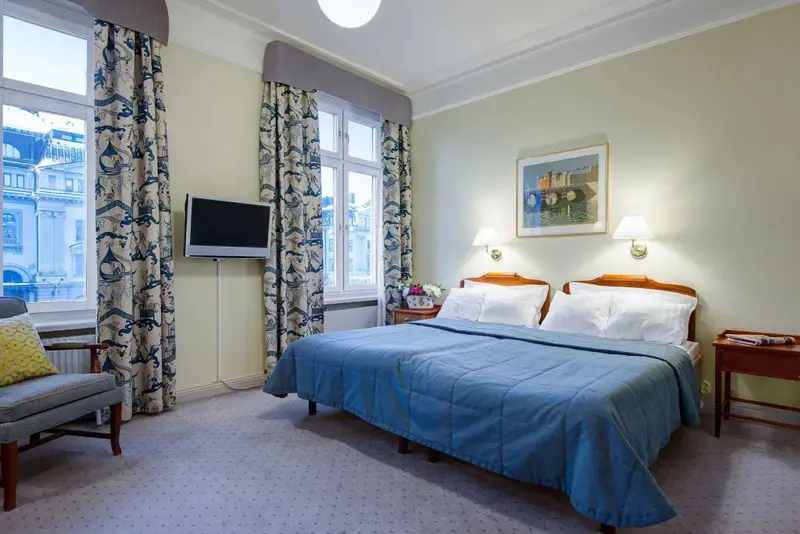 Une chambre lumineuse avec un grand lit et un fauteuil près de la fenêtre.
