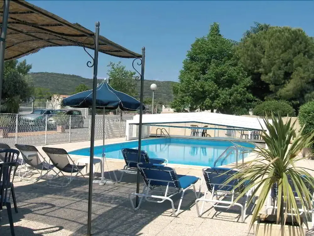 Transats bleus disposés autour d'une piscine ensoleillée sous un parasol.