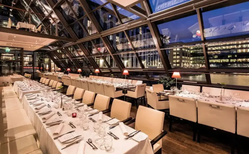 Une longue table est dressée dans une salle lumineuse avec une vue sur la ville.
