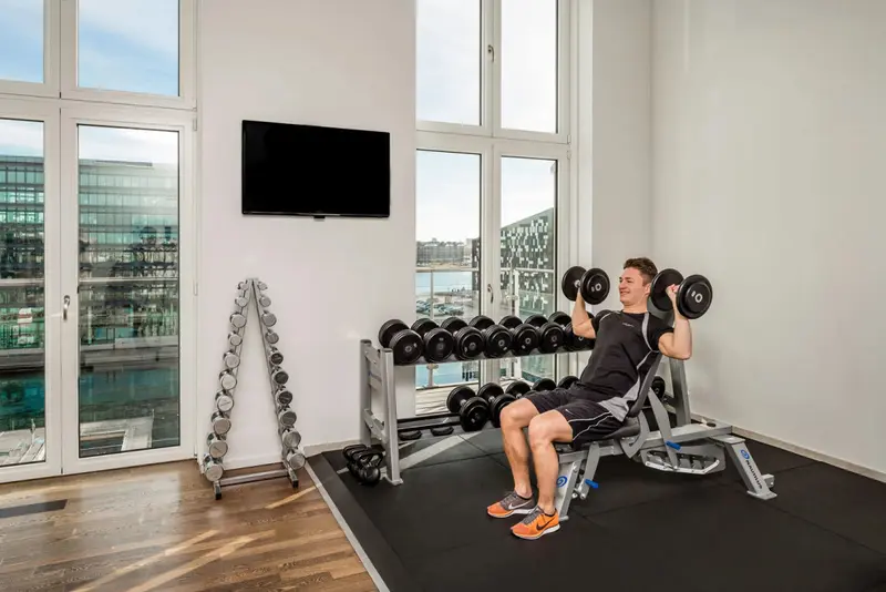 Une personne s'entraîne avec des haltères dans une salle de sport lumineuse.