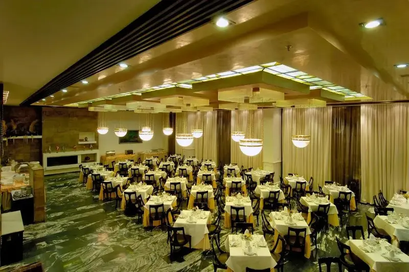 Une salle lumineuse est aménagée avec de nombreuses tables dressées pour un repas.