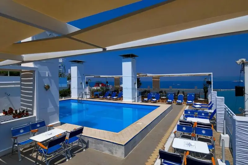 Une piscine bordée de chaises longues et de tables sous une pergola.