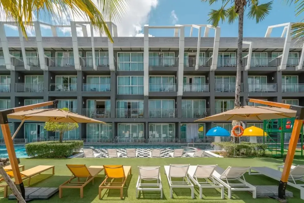Transats alignés devant une piscine et un bâtiment moderne.
