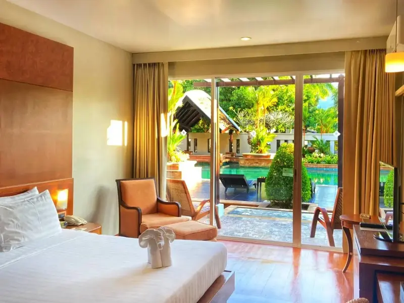 Une chambre lumineuse donne sur une piscine bordée de végétation tropicale.