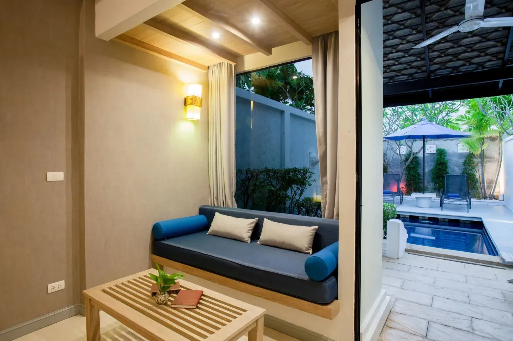 Un espace de détente intérieur avec un canapé et une table basse donne sur une piscine extérieure.
