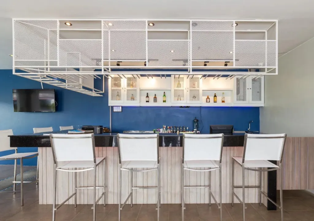 Un comptoir de bar moderne avec des tabourets blancs et des bouteilles exposées.