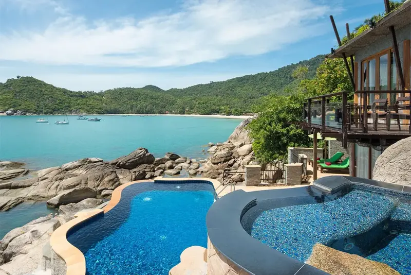 Piscine à débordement avec vue sur une baie turquoise et une végétation luxuriante.