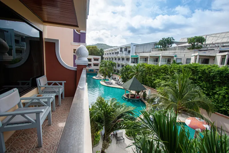 Vue d'un balcon avec des fauteuils donnant sur une piscine et une végétation luxuriante.