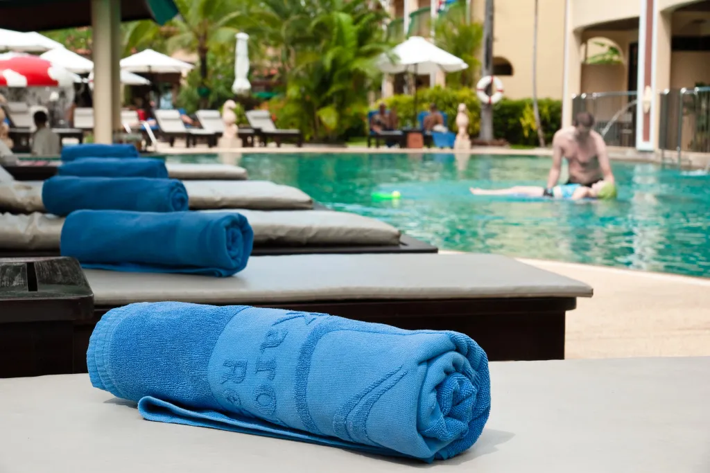Serviettes bleues roulées sur des transats au bord d'une piscine ensoleillée.