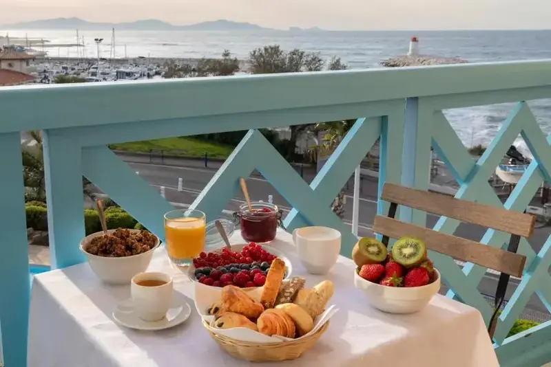 Une table est dressée pour le petit-déjeuner sur un balcon avec vue sur la mer et un port de plaisance.