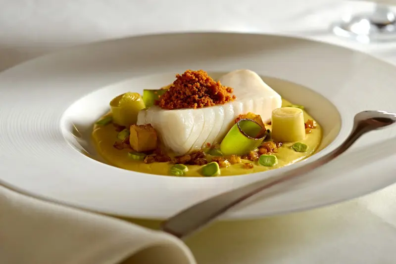Assiette raffinée avec un poisson blanc, des légumes et une sauce jaune.