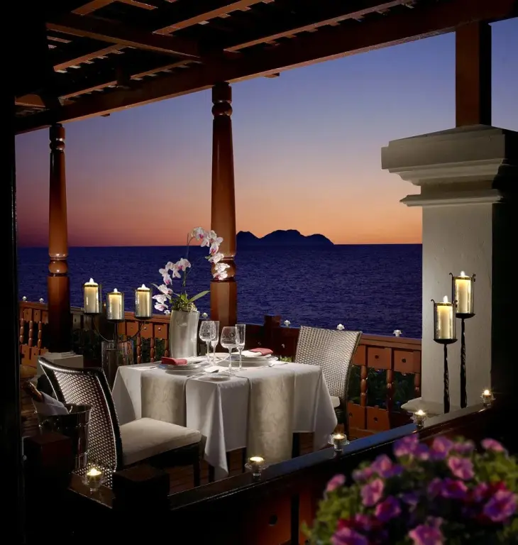 Table dressée pour un dîner romantique avec vue sur la mer au coucher du soleil.