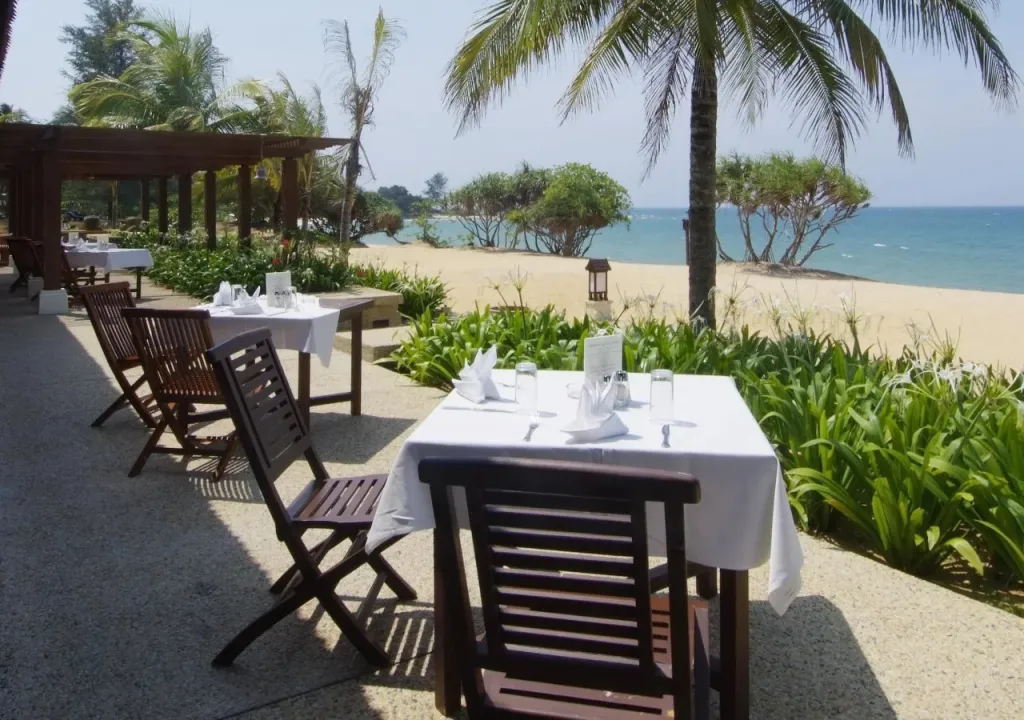 Tables dressées sur une terrasse ensoleillée face à la mer.