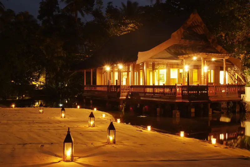 Un restaurant illuminé se reflète sur une plage de sable au crépuscule.