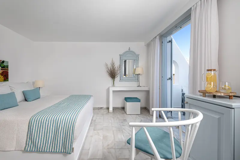 Une chambre lumineuse avec un lit recouvert d'une couverture rayée et un coin repos près d'une porte-fenêtre.