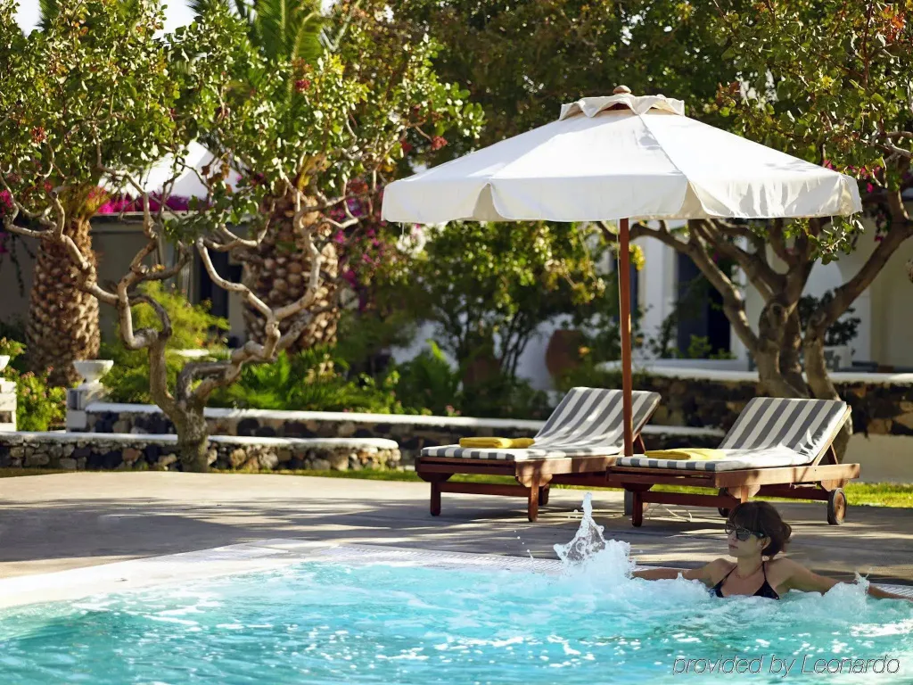 Une personne éclabousse l'eau dans une piscine bordée de chaises longues à l'ombre d'un parasol.
