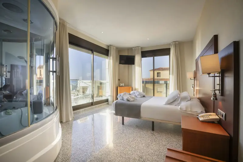 Une chambre lumineuse avec un grand lit et une salle de bain vitrée.