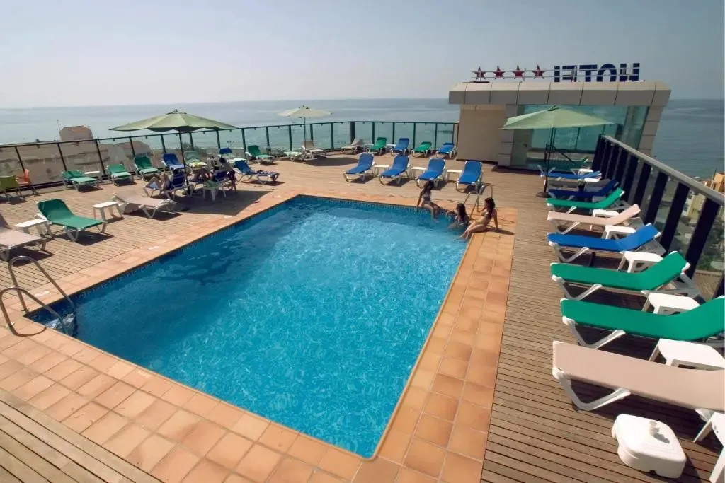 Une piscine rectangulaire entourée de transats sur une terrasse ensoleillée.