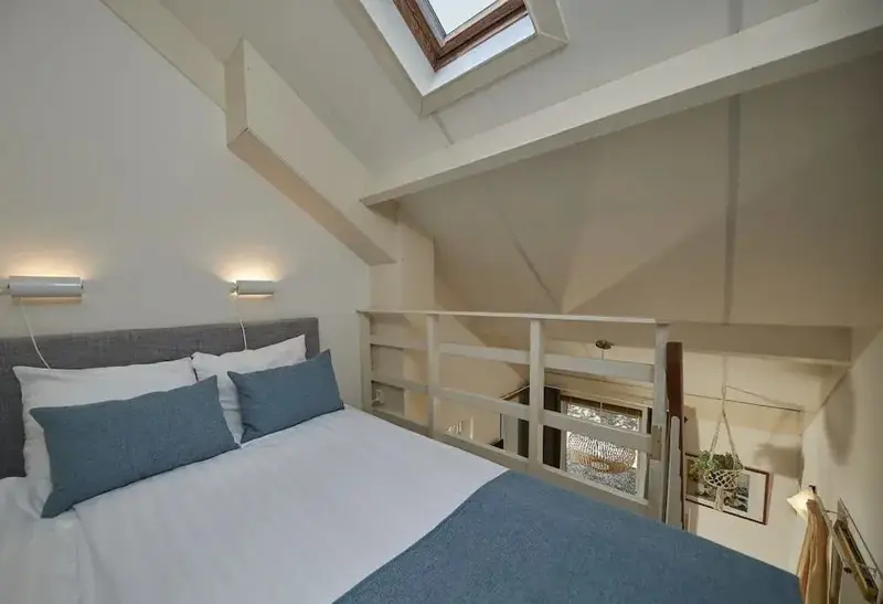 Une chambre mansardée lumineuse avec un lit double et une vue sur une galerie.
