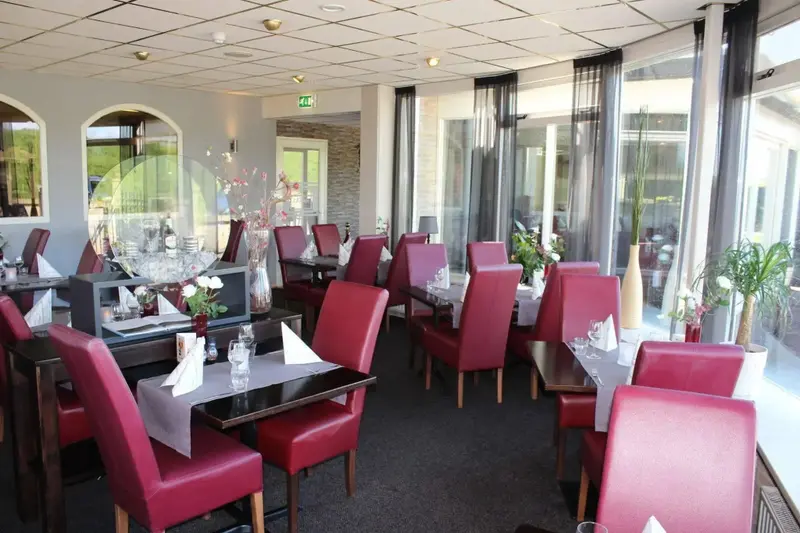 Une salle de restaurant lumineuse avec des tables dressées et des chaises rouges.