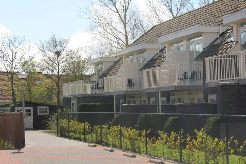 Logements blancs avec balcons donnant sur un jardin verdoyant.