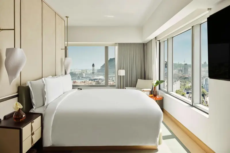 Chambre lumineuse avec un grand lit et une vue sur la ville.