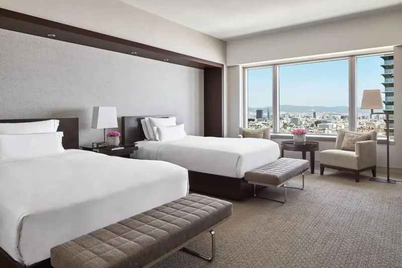 Chambre moderne avec deux lits et vue sur la ville.