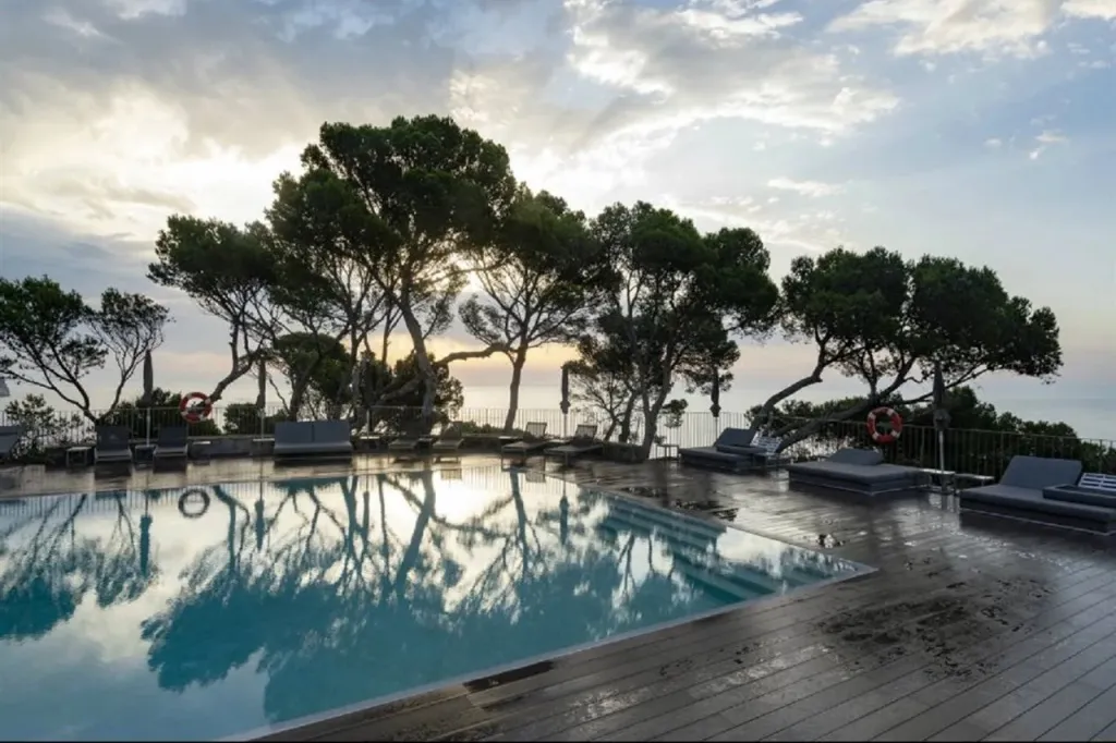 Une piscine rectangulaire avec des transats et des arbres en arrière-plan au coucher du soleil.