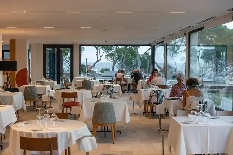Une salle lumineuse avec des tables nappées et une vue sur la mer.