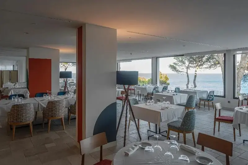 Une salle lumineuse avec des tables dressées face à une vue sur la mer.