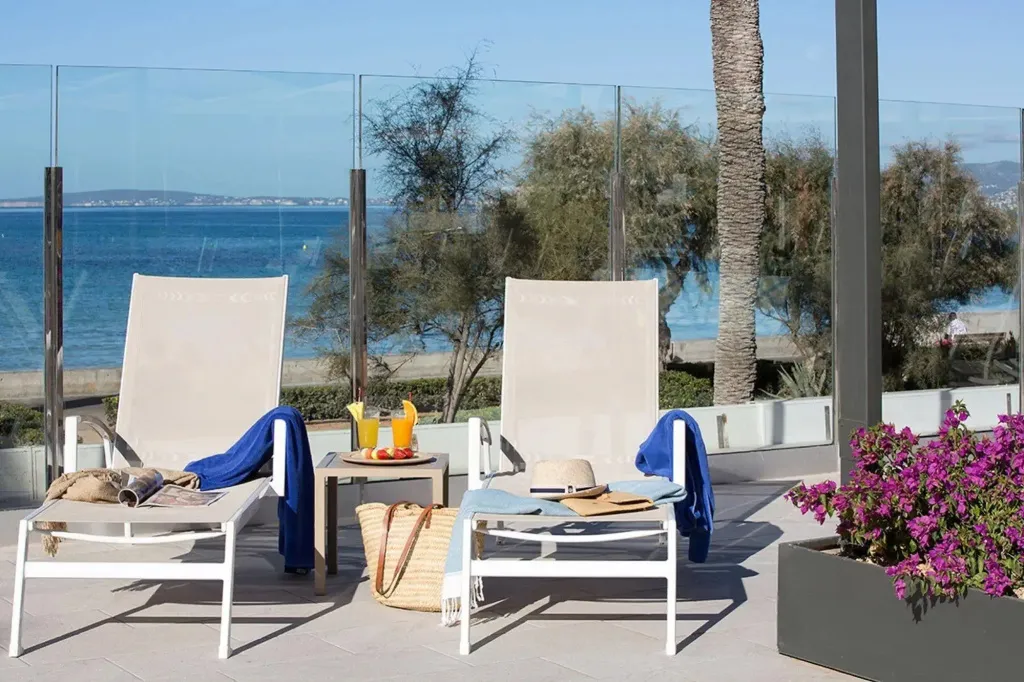 Deux transats blancs avec des magazines et des boissons sur une terrasse ensoleillée face à la mer.