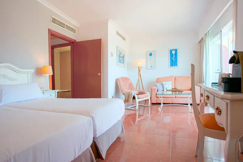 Une chambre lumineuse avec un lit blanc et un coin salon confortable.