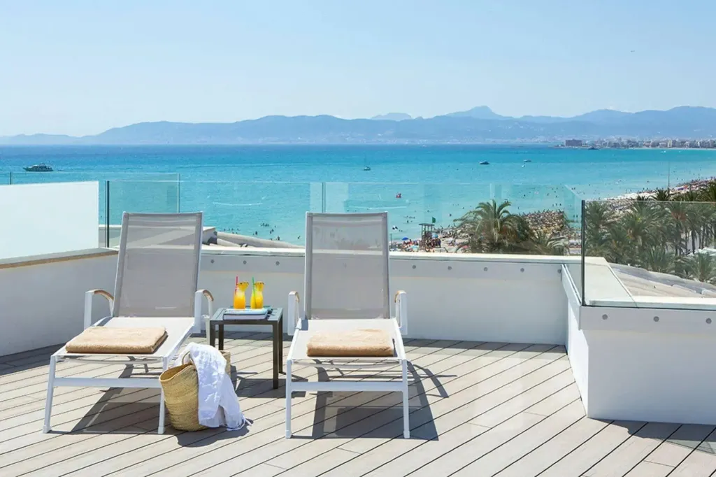 Deux transats avec une table basse et des boissons sur une terrasse en bois avec vue sur la mer.