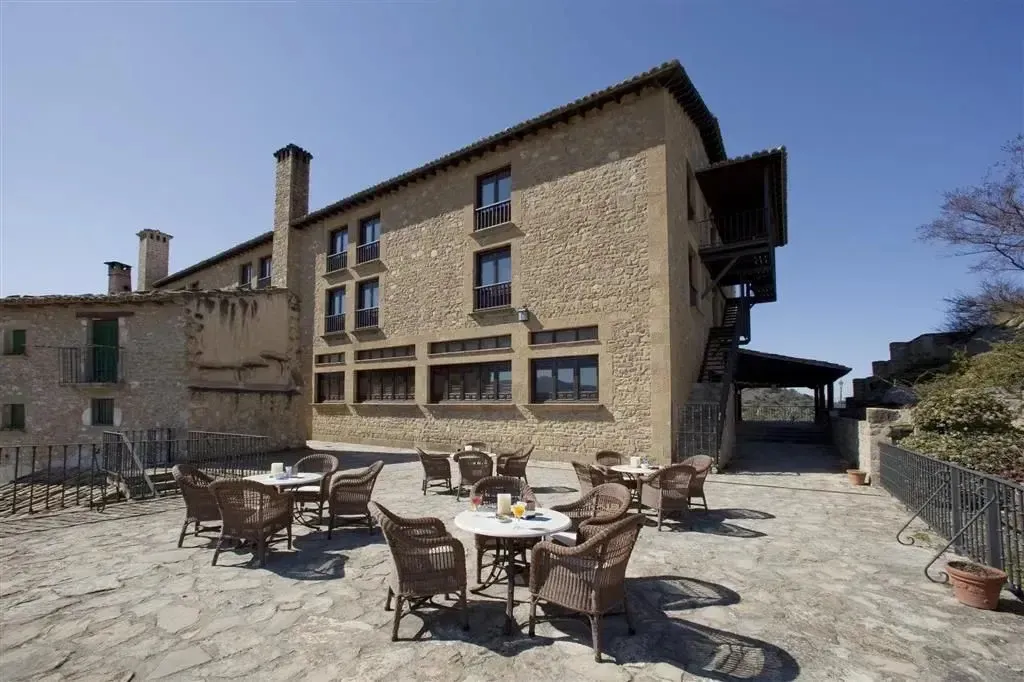Terrasse ombragée avec tables et chaises en osier devant un bâtiment en pierre.