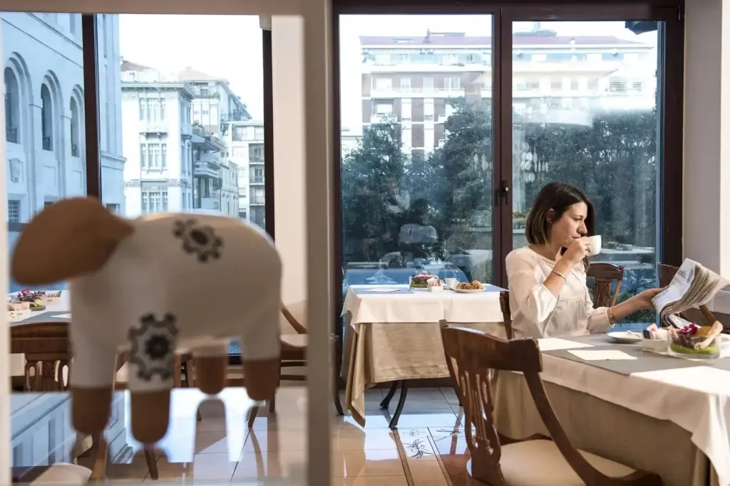 Une personne lit un journal tout en prenant une boisson à table dans une salle lumineuse.