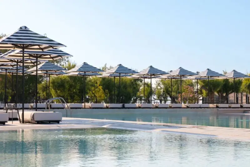 Une piscine rectangulaire bordée de transats sous des parasols rayés.
