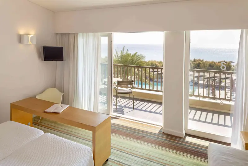 Une chambre lumineuse s'ouvre sur un balcon avec vue sur la mer.