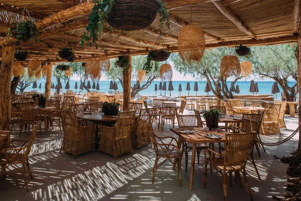 Terrasse ombragée avec tables et chaises en osier donnant sur la mer.