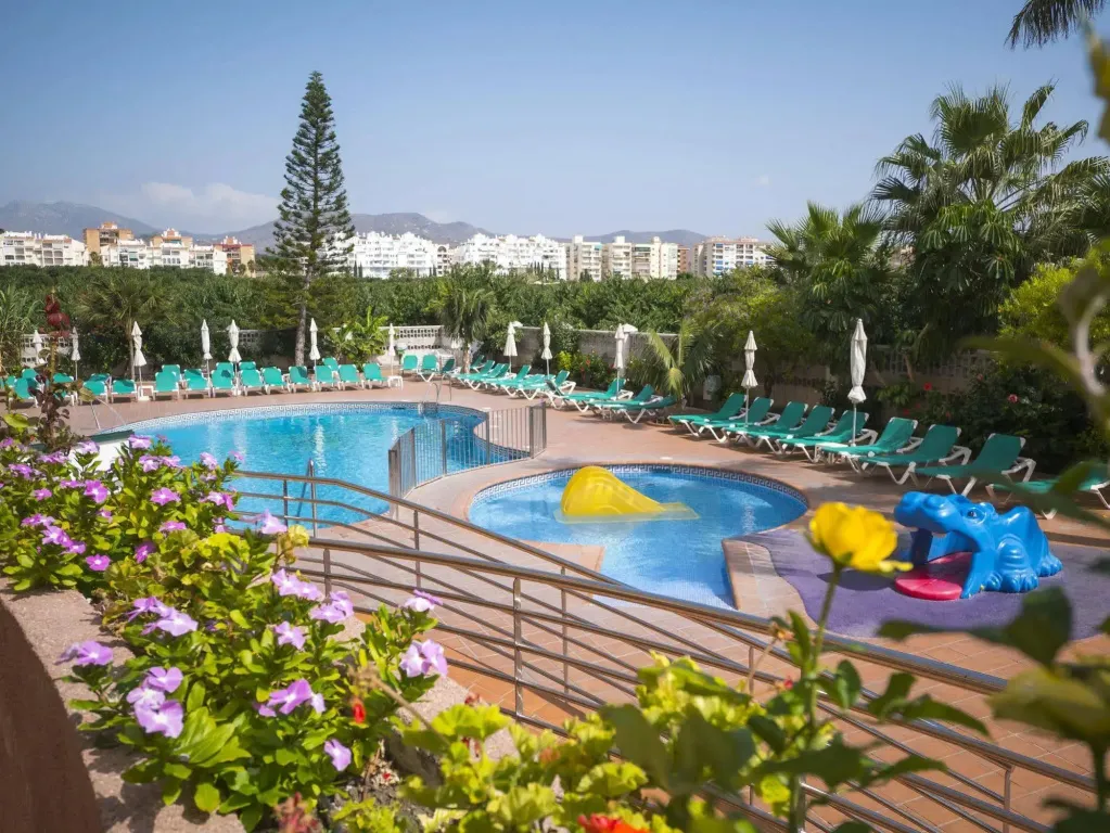 Piscine ensoleillée avec transats et jeux d'eau pour enfants.