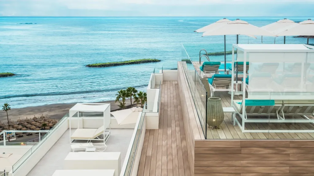 Terrasse en bois avec des transats blancs et des parasols vue sur la mer.