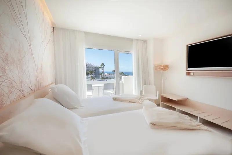 Une chambre lumineuse avec deux lits simples donnant sur une vue mer.