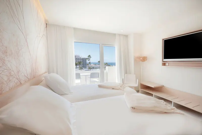Chambre lumineuse avec vue sur la mer par de grandes baies vitrées.