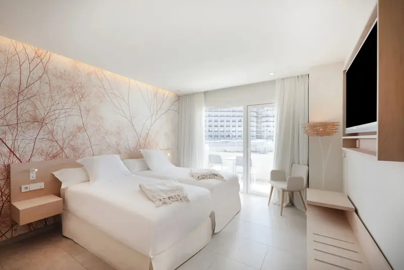 Chambre lumineuse avec deux lits simples et accès à un balcon.