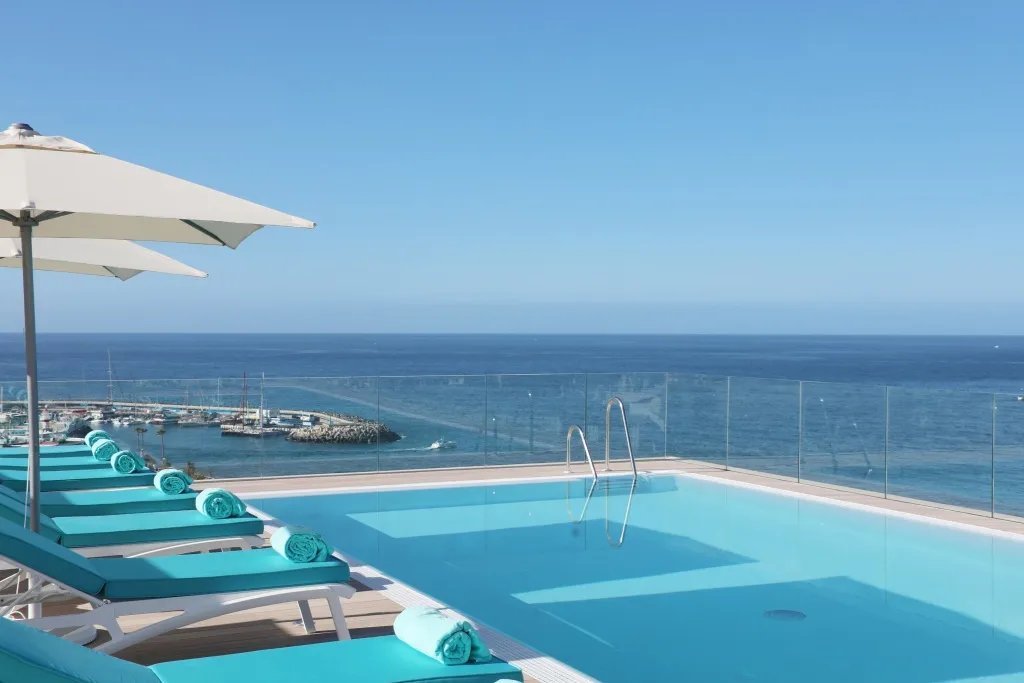 Transats bleus alignés au bord d'une piscine à débordement avec vue sur la mer.