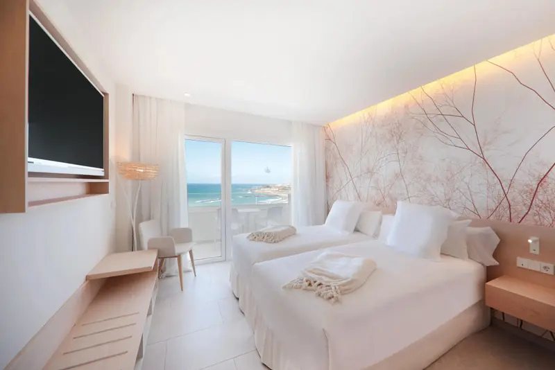 Chambre lumineuse avec deux lits simples et vue sur la mer.