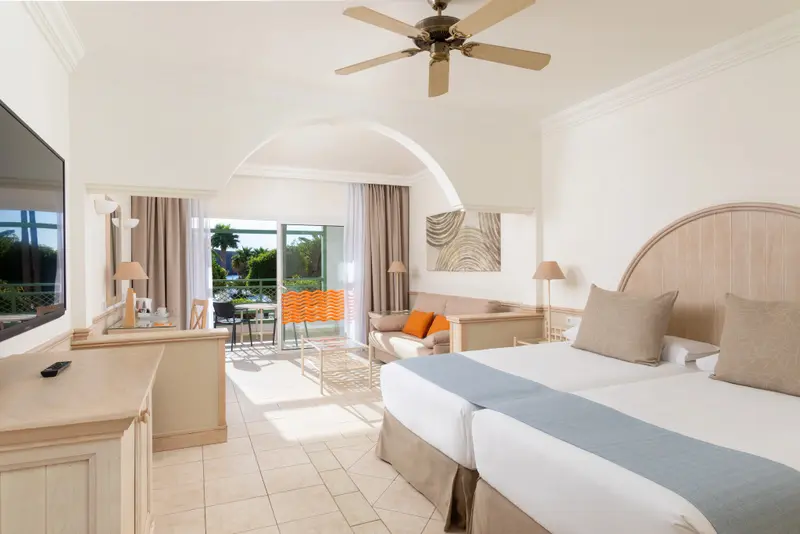 Une chambre lumineuse avec un lit double et un coin salon donnant sur une terrasse.
