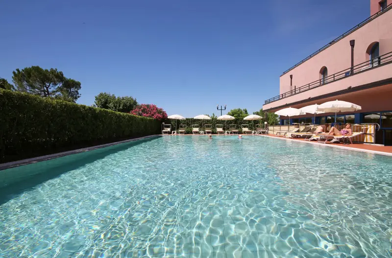 Une piscine rectangulaire bordée d'une haie verte et de transats sous des parasols.